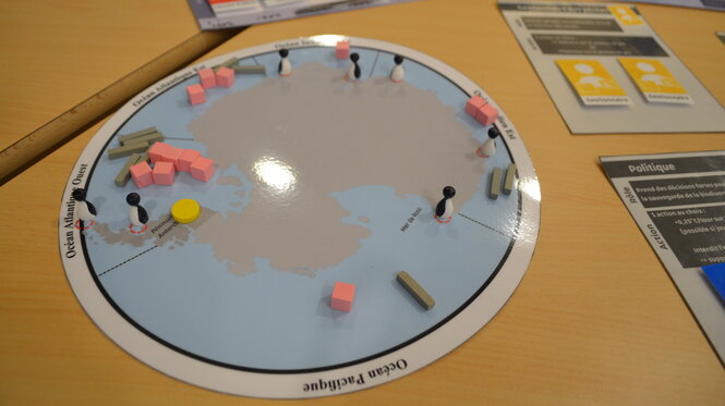 Plateau de jeu éducatif simulant des enjeux climatiques avec pions, cubes et cartes, utilisé lors d'un atelier pédagogique