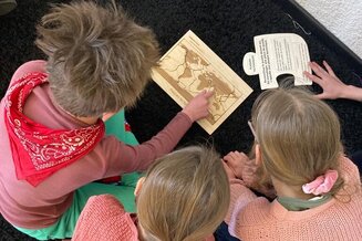 Trois élèves regardent une plaquette en bois représentant les continents