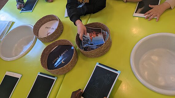 Élèves autour d'une table avec paniers en osier, cartes illustrées et tablettes d'écriture, participant à l'atelier